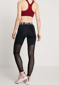 Svarta leggings med meshnätpaneler som har ett litet mönster, hög midja med logotyp, i kombination med en vinröd sport-bh och ljusrosa sneakers.