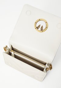 Λευκή δερμάτινη τσάντα χειρός με μεταλλικό χρυσό κυκλικό διακοσμητικό και τσέπες με φερμουάρ. Διαθέτει κουμπιά σνάπ και ραμμένα διακοσμητικά στοιχεία στο εξωτερικό.