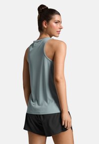 Canotta atletica grigio chiaro senza maniche con finitura texturizzata e scollatura rotonda, abbinata a pantaloni corti neri. Logo discreto sul retro.