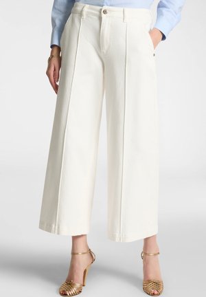 Wide-leg trousers in white cotton fabric, featuring a high waist, front pleats, and side pockets. Paired with strappy gold high-heeled sandals.