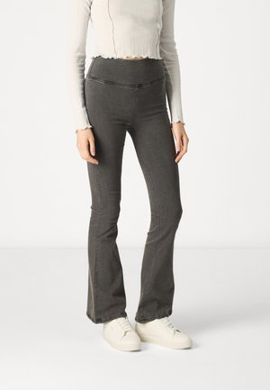 Vaqueros acampanados grises para mujer con cintura alta, que presentan una textura de denim suave y un detalle de costura mínimo, combinados con zapatillas blancas.