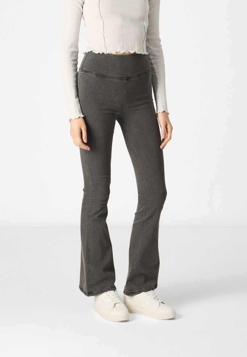 Ženske sivo ispuhane traperice s visokim strukom, s glatkom denim teksturom i minimalnim detaljima šivanja, u kombinaciji s bijelim tenisicama.