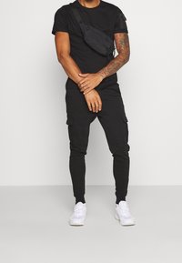 Svart rundhalsad t-shirt, cargo-byxor med fickor och vita sneakers. Inkluderar en svart axelväska, allt för att skapa en strömlinjeformad look.