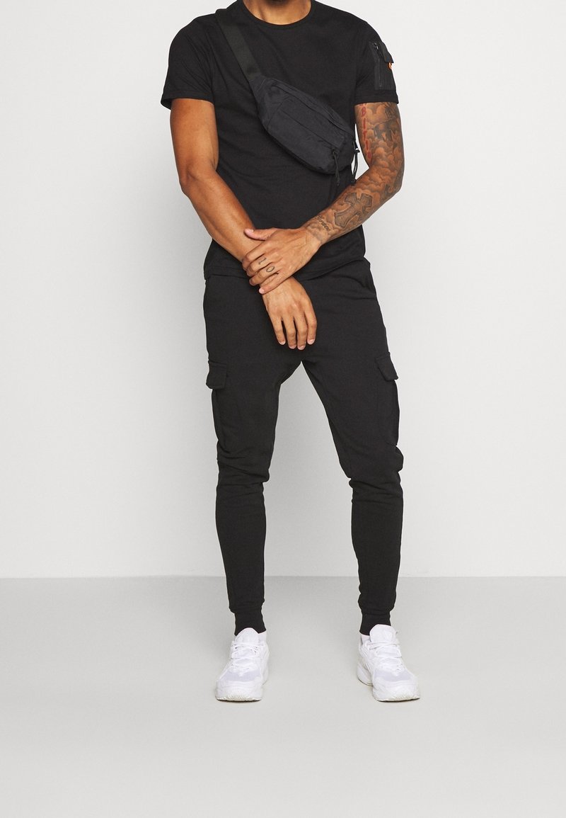 Svart rundhalsad t-shirt, cargo-byxor med fickor och vita sneakers. Inkluderar en svart axelväska, allt för att skapa en strömlinjeformad look.