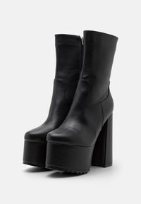 Bottes à plateforme en cuir noir avec talon bloc haut, texture lisse, bout arrondi et fermeture éclair latérale.