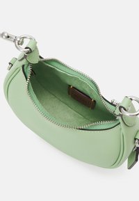 Petit sac à main vert clair avec fermeture éclair argentée, ouvert pour montrer l’intérieur en tissu doux et la pièce de cuir de la marque à l’intérieur.