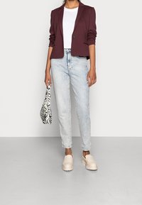 Blazer bordeaux sur mesure porté sur un t-shirt blanc, jean bleu clair, chaussures à plateforme beiges et sac à main noir et blanc à motif zèbre.