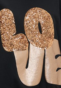 T-shirt preta com texto audacioso "LOVE" em lantejoulas douradas e glitter. O design incorpora texturas brilhantes e acabamentos contrastantes.