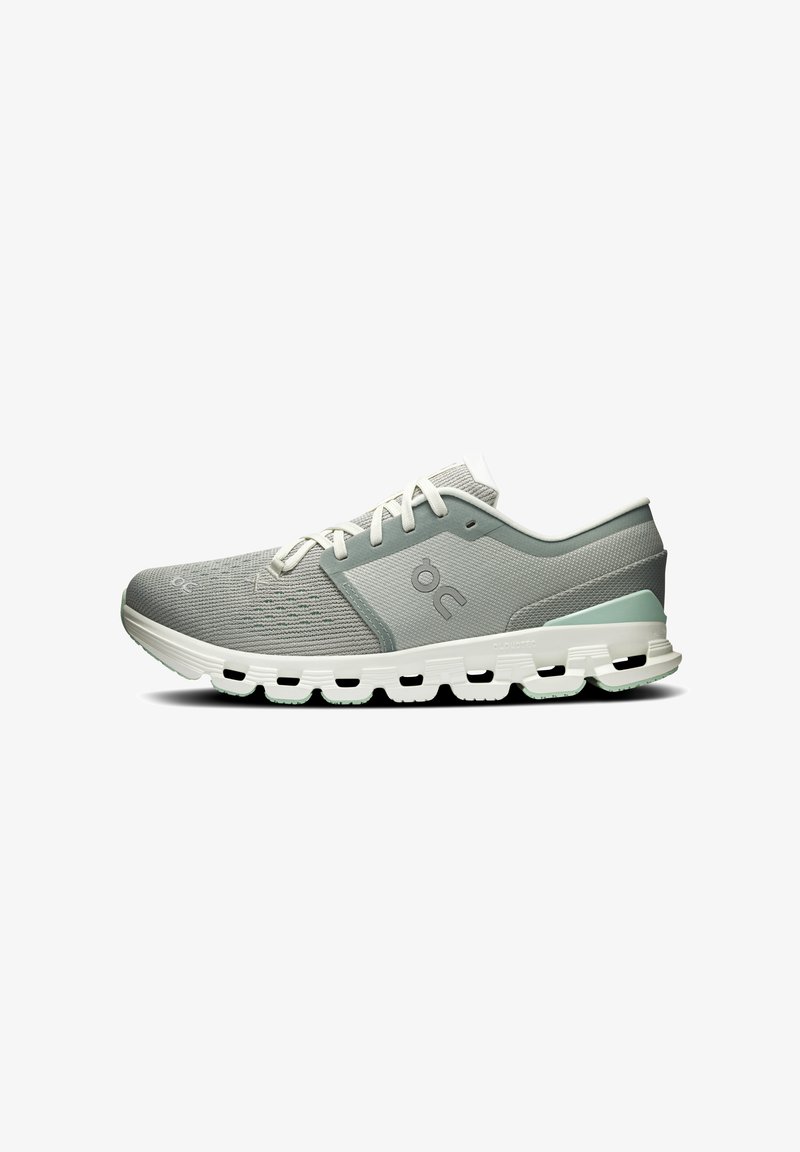 Chaussure de sport gris clair avec lacets blancs, semelle blanche coussinée avec découpes noires, et accent subtil vert au talon, vue de côté.