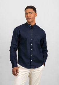 Camicia button-up di un blu navy scuro con colletto alla cinese, maniche lunghe e una tasca sul petto. Presenta bottoni bianchi e un tessuto testurizzato.