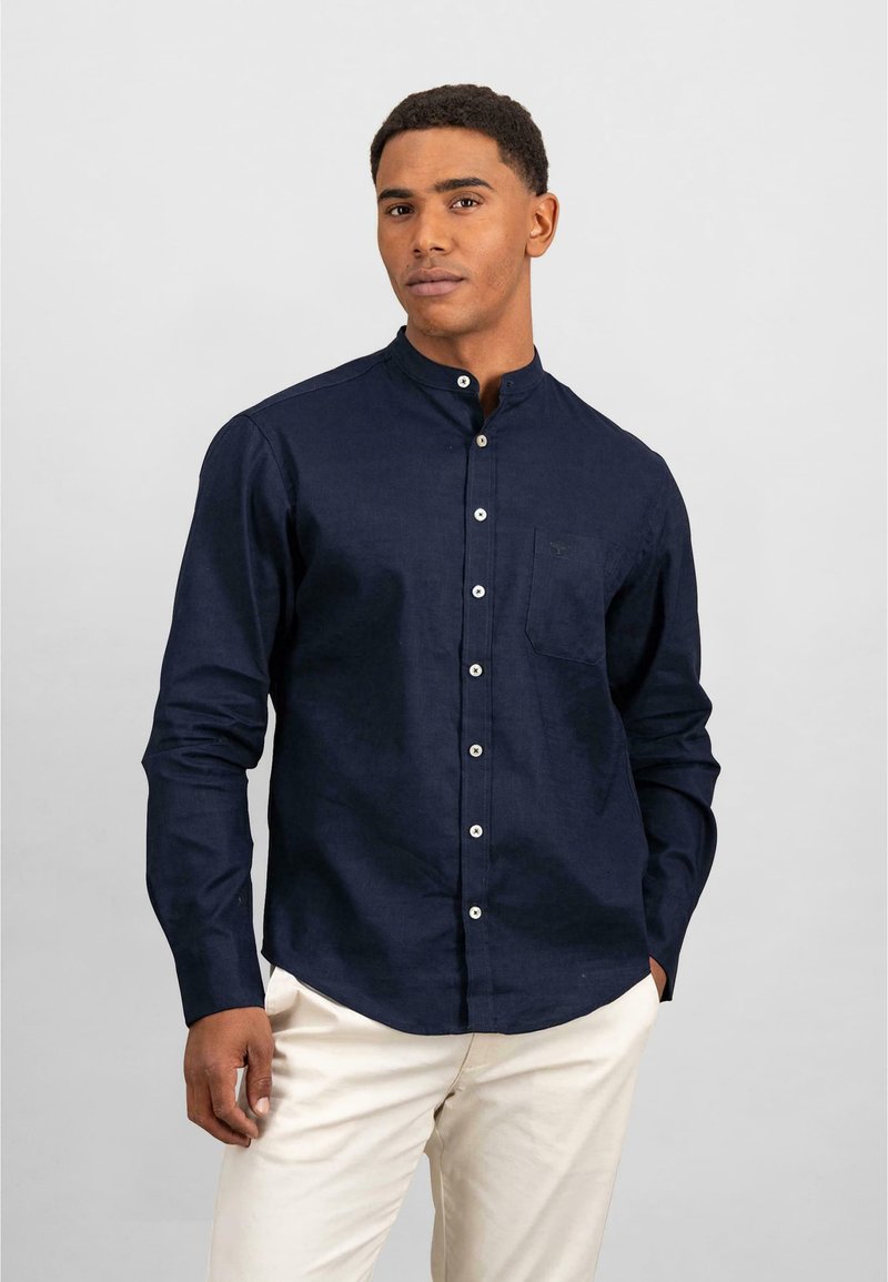 Camicia button-up di un blu navy scuro con colletto alla cinese, maniche lunghe e una tasca sul petto. Presenta bottoni bianchi e un tessuto testurizzato.