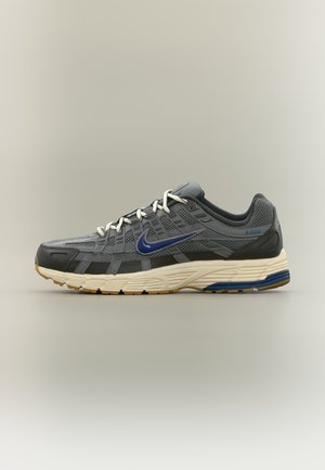 Chaussure de course Nike grise et noire avec logo swoosh bleu, lacets blancs et semelle beige avec découpes bleu et marron.