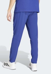 Niebieskie spodnie sportowe z lekkiego, gładkiego materiału z zamkami u dołu nogawek, zestawione z białymi trampkami z czarnymi paskami.
