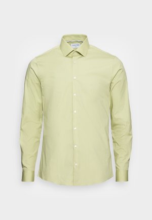 Jasnozielona koszula z długim rękawem wykonana z bawełny. Posiada kołnierzyk na guziki oraz listwę na guziki z przodu z białymi guzikami. Odzież ma gładką fakturę.