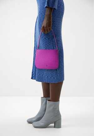Une personne en robe bleue texturée tient un petit sac à main en cuir gaufré crocodile violet, portant des bottines en cuir gris clair avec des talons carrés.