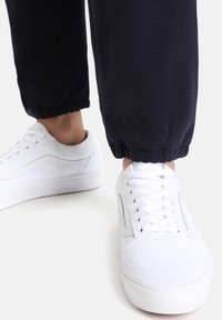 Vita snörskor i lace-up-stil med en slät läderövre och gummisula, kombinerade med mörkblå uppvikta joggerbyxor, som visar en enkel design.