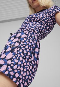 Vestido PUMA multicolorido con un diseño ajustado que presenta un estampado abstracto de leopardo en azul y rosa, mangas cortas y una cintura ceñida.
