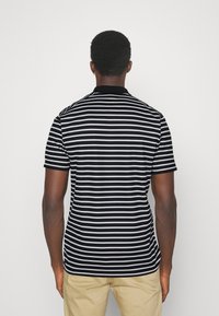 Svartvit randig kortärmad polo skjorta med svart krage. Tyget verkar lätt och har en mjuk textur.