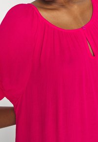 Fuchsia blouse with short, puff sleeves and a keyhole neckline. The fabric is lightweight, textured, and drapes loosely. Features a small button.