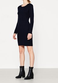 Robe en tricot côtelé marine avec un col rond et des manches longues, assortie à des bottines noires à talons épais et à texture lisse.