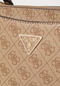 Brązowa torebka o teksturowanej powierzchni z wzorem w diamenty oraz złotym akcentem w kształcie trójkąta z logo. Zamek błyskawiczny i smukły profil.