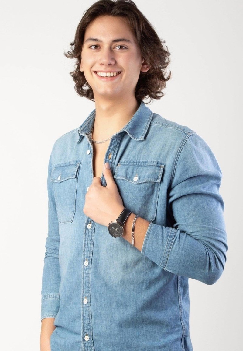 Chemise en denim avec un design à boutons, manches longues et deux poches poitrine. Les accessoires comprennent une montre avec un bracelet noir et un bracelet en argent.