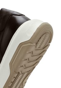 Zapatilla de cuero marrón con suela de goma blanca. La suela presenta un patrón de dibujo en zigzag. El zapato tiene una textura suave y detalles de diseño mínimos.