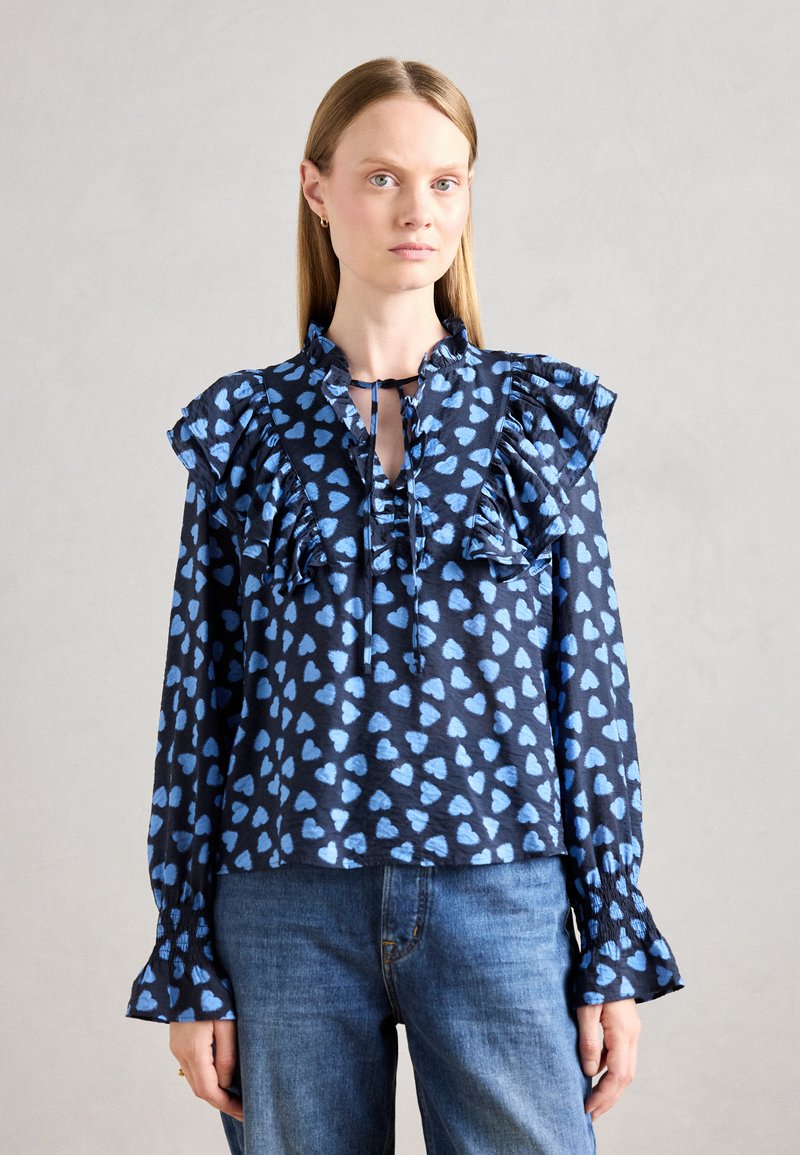 Blusa a maniche lunghe blu navy con motivi a cuori azzurri, spalline arricciate e scollatura con fiocco; realizzata in tessuto leggero.
