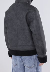 Szara kurtka z sztucznej skóry z czarnymi mankietami i dołem wykończonym polarowym, charakteryzująca się strukturalnym fasonem i minimalną liczbą szwów.