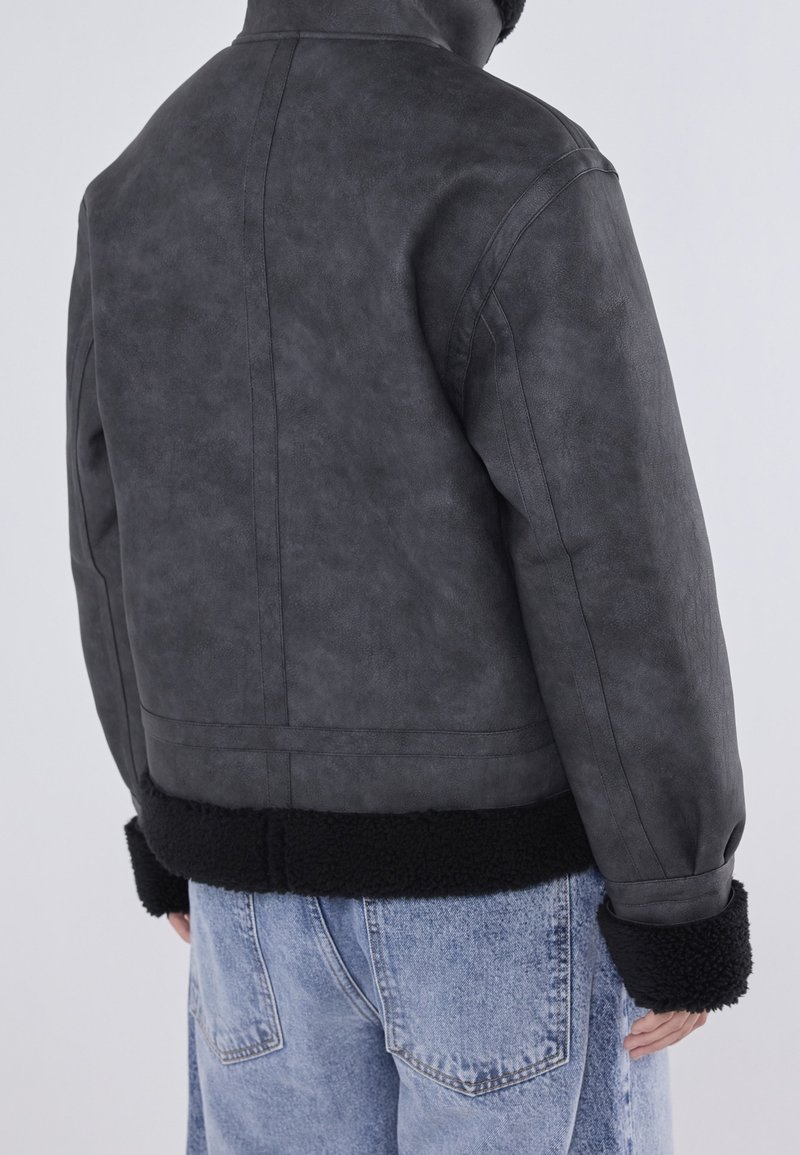 Szara kurtka z sztucznej skóry z czarnymi mankietami i dołem wykończonym polarowym, charakteryzująca się strukturalnym fasonem i minimalną liczbą szwów.