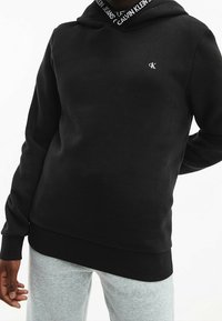 Felpa nera con cappuccio realizzata in morbido misto cotone, caratterizzata da un logo sul petto e un colletto a coste con marchio. I polsini e l'orlo sono aderenti.