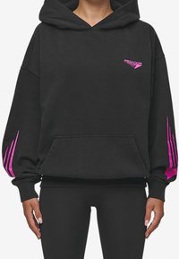 Černá mikina s velkou přední kapsou, zdobená růžovými grafickými akcenty na rukávech a logem na hrudi. Tkanina vypadá měkce a teple.