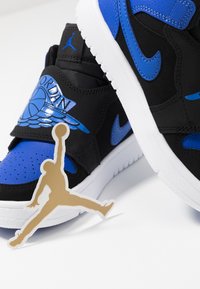 Černé a modré sportovní boty s texturovaným svrškem, bílou podrážkou a zlatou nášivkou loga Jordan s skákající siluetou.