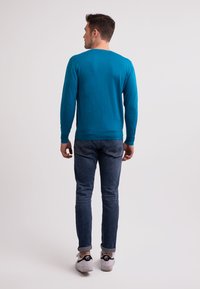 Turkos långärmad tröja med rundad halsringning och stickad struktur. Matchad med mörka denimjeans och vita sneakers. Bakvy.