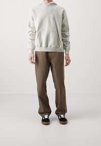 Jasnoszary sweatshirt z kapturem, z przednią kieszenią typu kangur, zestawiony z brązowymi spodniami i czarnymi trampkami z białymi sznurowadłami i gumową podeszwą.