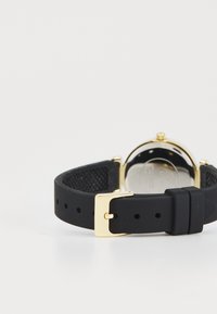 Bracelet de montre en silicone noir avec une boucle en métal doré ; présente un design texturé et un boîtier rond avec un dos réfléchissant.