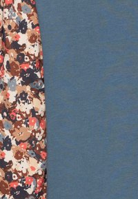 Puuvillapaita, jossa on sininen vartalo ja kukkakuosi yhdellä puolella. Kukkien värit ovat punainen, ruskea ja sininen, vaalean kermaisen taustan päällä.