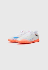 Une paire de chaussures de sport blanches avec des semelles orange, des accents bleu et orange à motifs, des lacets blancs et un logo Puma noir sur le talon.
