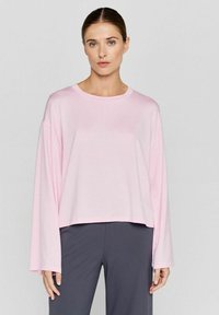 Rosa Langarm-T-Shirt mit Rundhalsausschnitt, taillierter Schnitt und glatter, weicher Textur. Getragen mit dunkelgrauen Hosen.