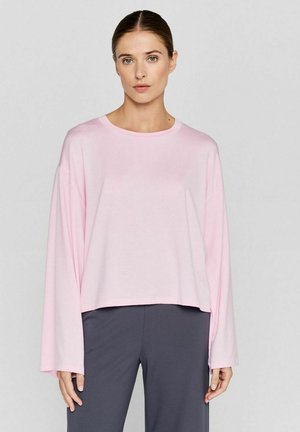 Roze langslavige T-shirt met een ronde halslijn, cropped snit en een gladde, zachte textuur. Draagt met donkergrijze broek.