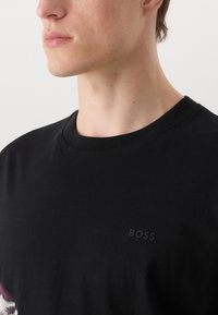 Črna bombažna majica s krožnim izrezom, ki ima subtilno embosirano "BOSS" logo na levi strani. Gladka tekstura, klasičen kroj.