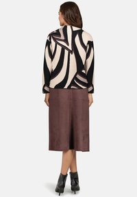 Czarny i beżowy sweter w abstrakcyjny wzór z długimi rękawami, noszony na brązowej zamszowej spódnicy do kolan, w zestawieniu z czarnymi botkami na obcasie.