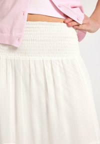 Hvid nederdel med smocket talje og en plisseret design, lavet af let materiale, kombineret med en lyserød cardigan.
