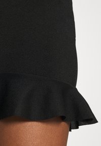 Černá sukně z texturované látky s volánovým lemem. Materiál vypadá hladce a nabízí těsný siluetu.