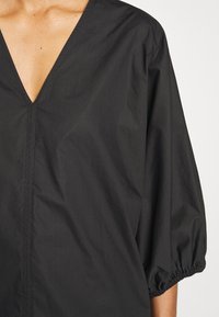Blusa nera con scollatura a V e maniche a sbuffo. Realizzata in materiale leggero, presenta dettagli di cucitura sottili e polsini arricciati.