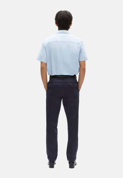 Lichtblauwe shirt met korte mouwen, marineblauwe broek en zwarte schoenen. De broek heeft dubbele achterzakken met knopenflappen. Eenvoudig ontwerp.