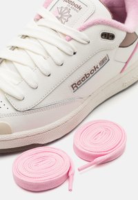 Sneaker bianca in pelle con accenti rosa, dotata di lacci testurizzati, linguetta imbottita e suola in gomma. Include due rotoli di lacci rosa.