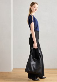 Dunkelblaues Oberteil mit metallischen Hardware-Details an den Schultern, kombiniert mit hochgeschnittenen schwarzen Hosen und einer strukturierten schwarzen Lederhandtasche.