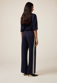 Completo sportivo navy composto da una maglia morbida e pantaloni a gamba larga con strisce laterali bianche, abbinato a décolleté nere a punta.