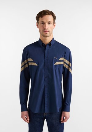 Marineblaue Hemdjacke mit einem klaren Kragen, versehen mit beigen geometrischen Akzenten auf Brust und Schultern, gefertigt aus glattem Stoff.